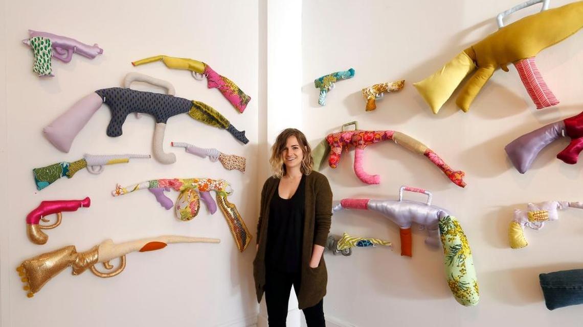 Cat Wentworth, director of Institute 193, posed March 22 with an exhibit of sewn and stuffed sculptures by Natalie Baxter, many of which are modeled after actual weapons used in recent U.S. mass shootings. The gallery is at 193 North Limestone St. in Lexington, Ky.