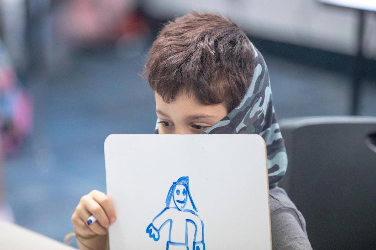 Logan Sherman holds up his drawing to a web camera to show his work to his teacher during a virtual class while working in a learning pod at Salvation Army in Lexington, Ky., Monday, Sept. 14, 2020.