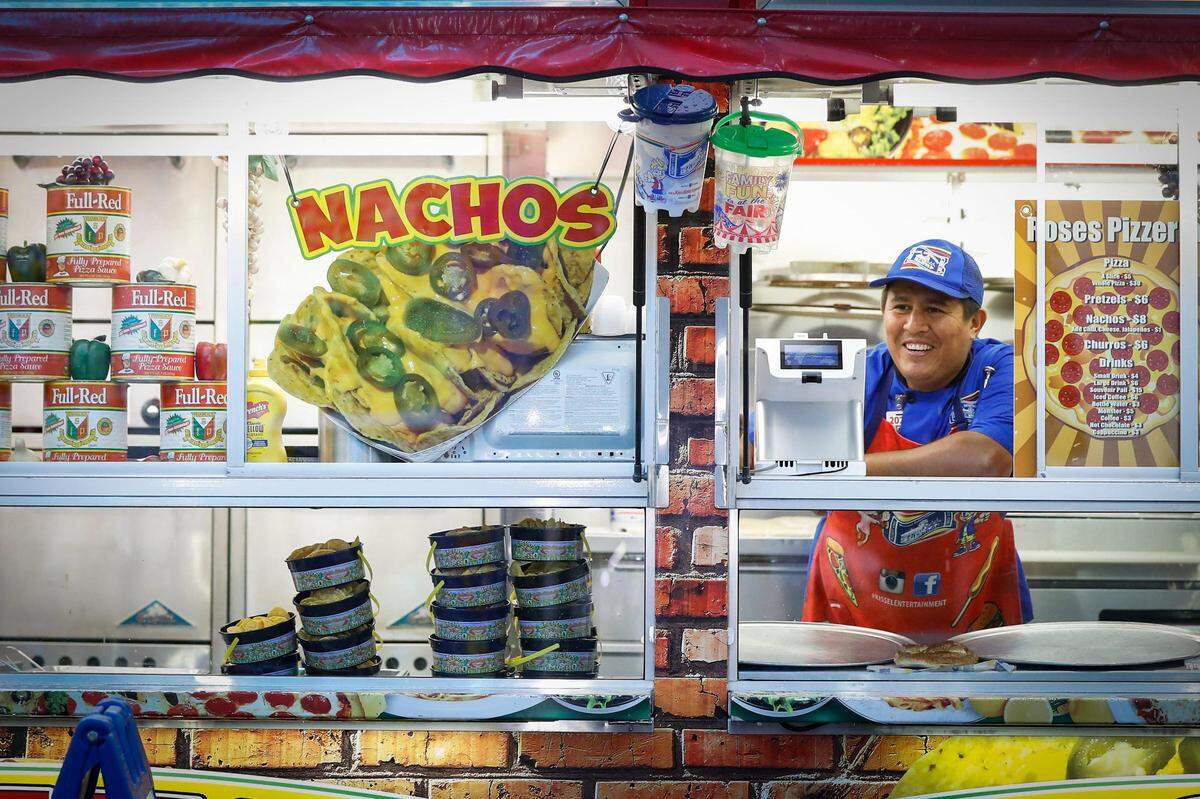 Carlos Milla jokes with a customer while offering slices of pizza at the Lexington Lions Club’s Bluegrass Fair at Masterson Station Park in Lexington, Ky., Friday, June 11, 2021.