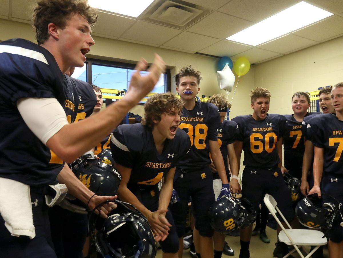 Sayre’s Nick Clark, left, and Jack Foster, clapping, rallied the Spartans in the locker room before the program played its first football game since 1977.
