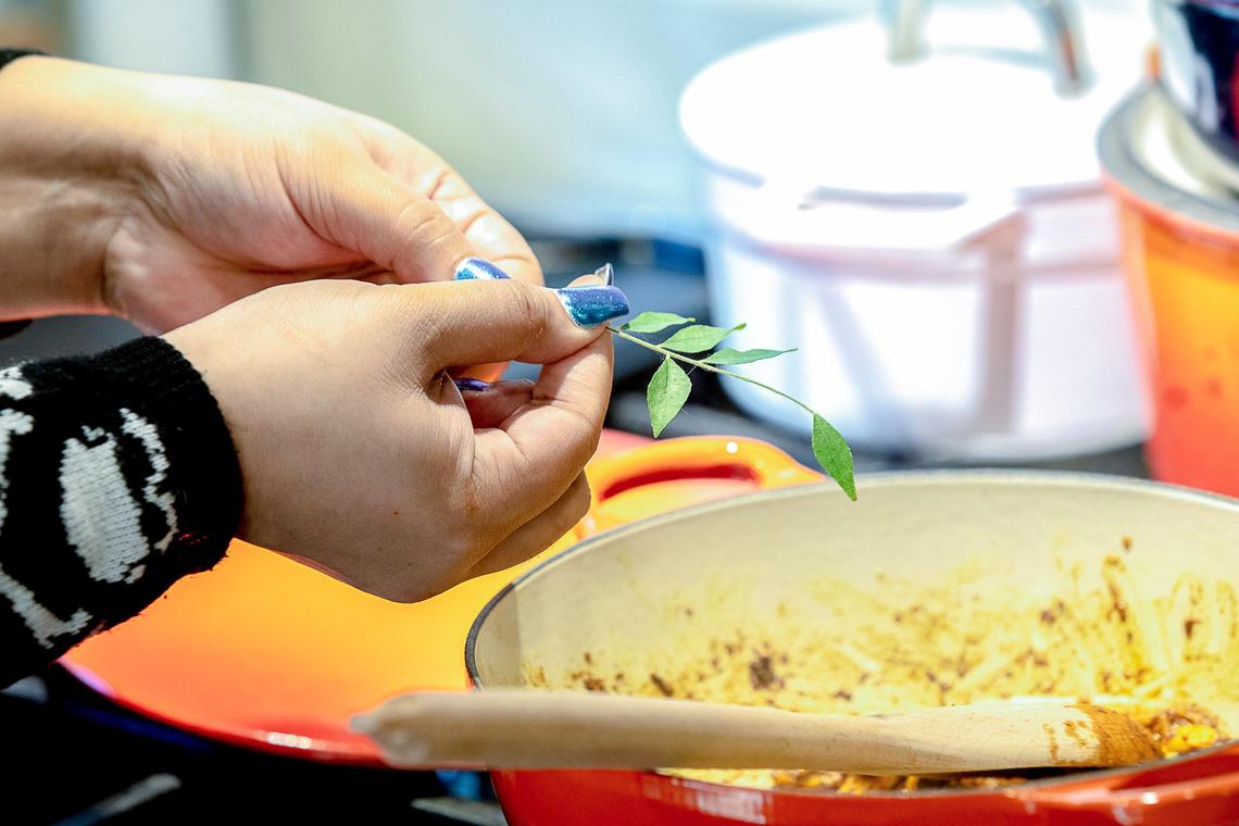 Samantha Fore adds fresh curry leaves she grew to a mango curry at her home in Lexington. She often cooks in her home for friends and guests.