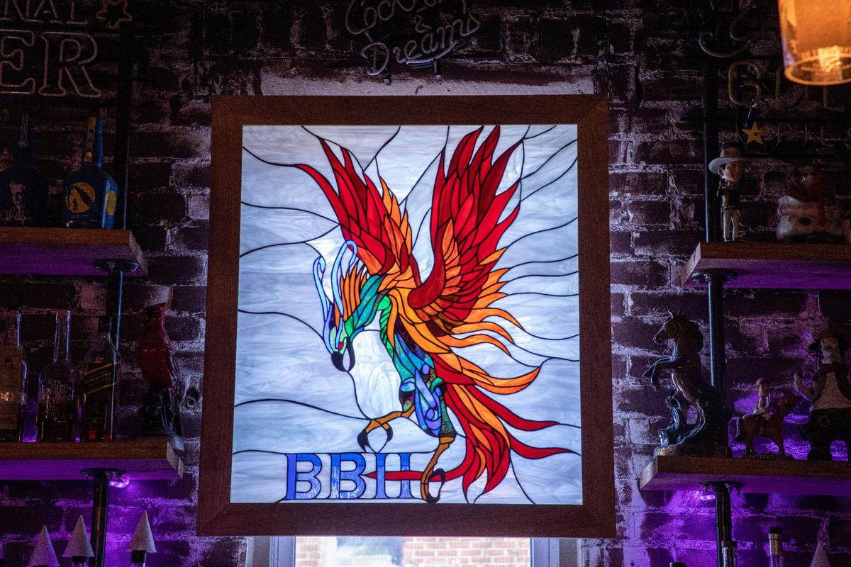 A stain glass piece of a phoenix hangs over a window above the bar at Bluegrass Barrel House. The piece was made for the current owners Raela and Anthony Phoenix by a long-time friend, Tim Fifield.