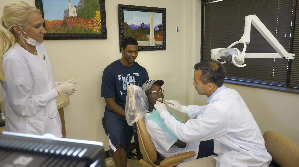 Dr. Pada Chalothorn, right, and assistant Kristin Potter showed off the results of dental work done on UK basketball fan William Bolden. Former Wildcat Terrence Jones sat behind Bolden. Jones befriended Bolden after watching him play pickup games on the courts near Wildcat Lodge.  