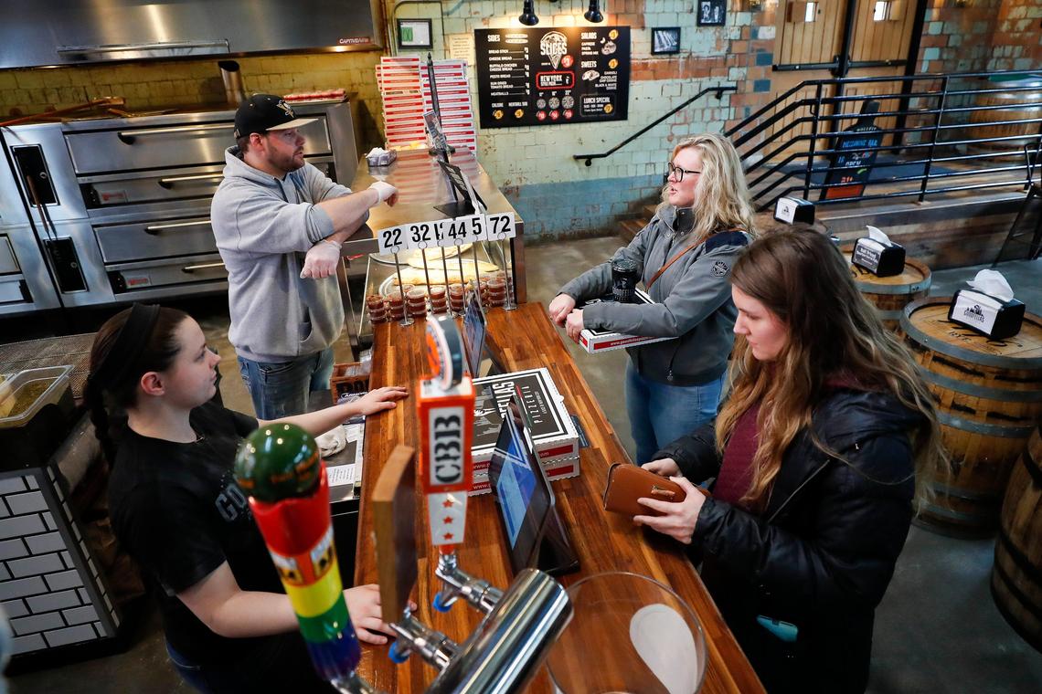 Goodfellas Pizzeria employees Devin Paulding, upper left, and Jessica Jones, lower left, handle takeout orders Saturday from Heather Thomas, upper right and Michaela Rogers the Distillery District location. Alex Coats, co-owner, said they are “down about 60-70 percent from what we normally operate at.”