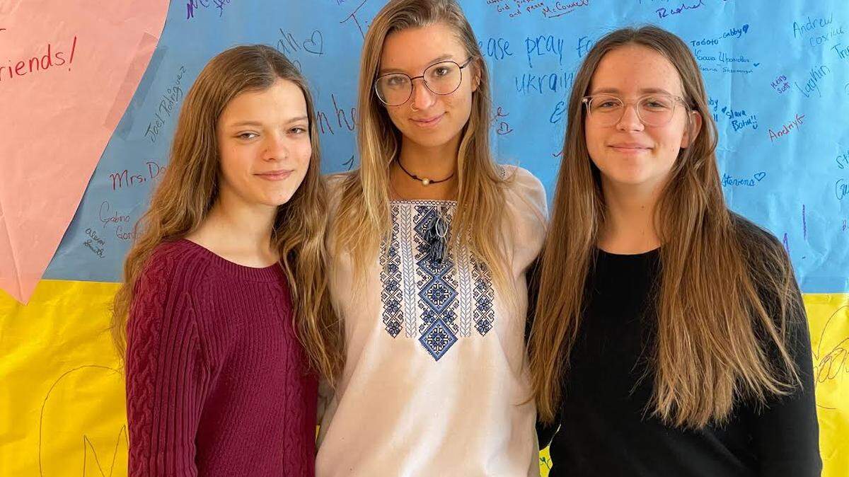 From left, students Yuliaa Ligvin, Angelika Yarynka, and Rachel Chabaruk standing in front of a Ukrainian flag made by students at West Jessamine High School in Nicholasville, Ky.