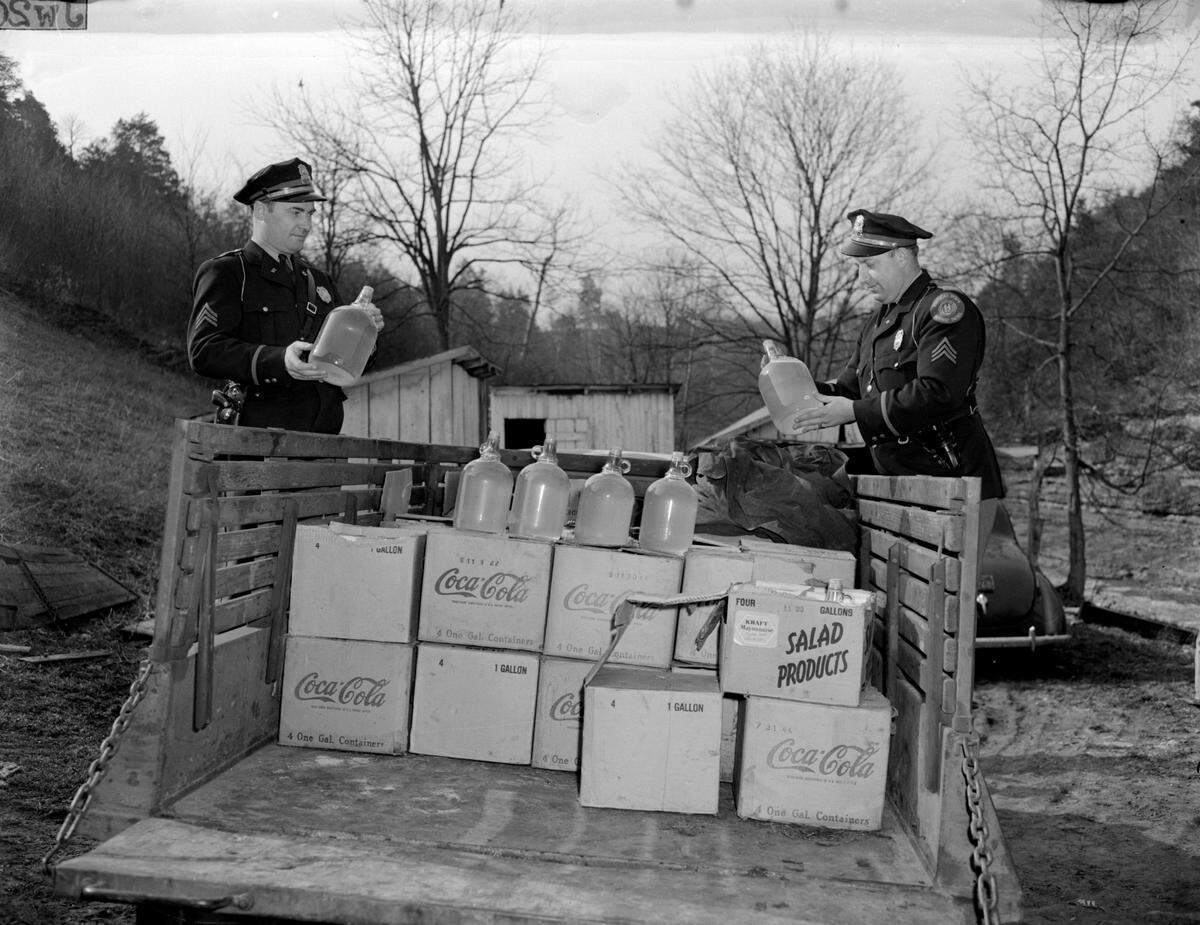 Two Kentucky Highway Patrol officers looked over a load of moonshine confiscated near Frankfort in 1945.