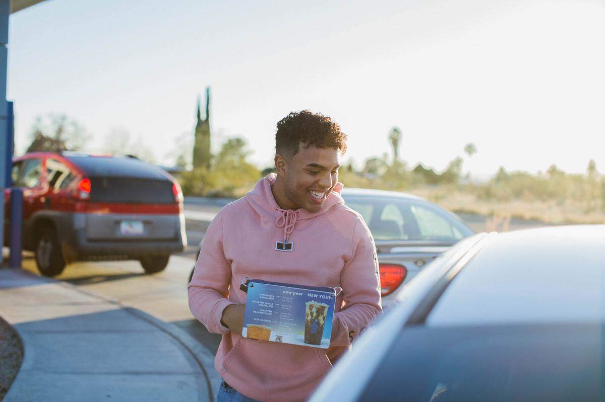 A “broista” takes an order at a Dutch Bros Coffee drive-thru, where passionate fans line up for coffee.