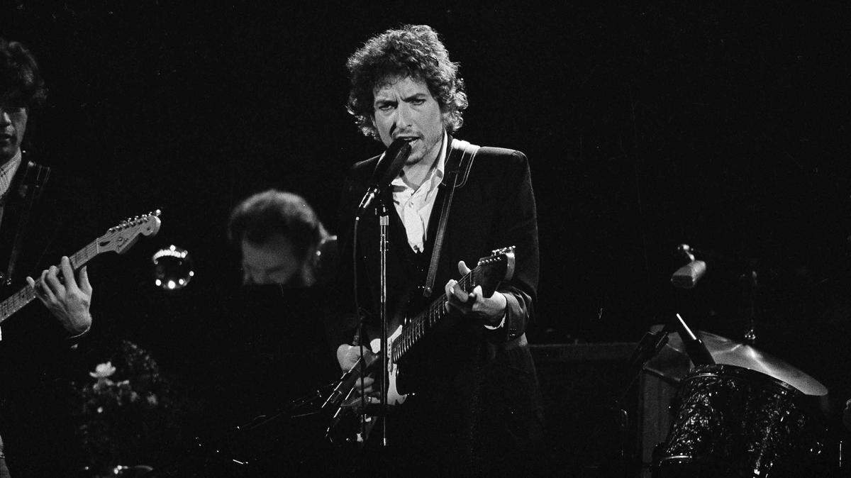 Musician Bob Dylan belts out a tune as members of The Band, Robbie Robertson, partially hidden left, and Garth Hudson, background center, accompany him during a concert at the Forum in Los Angeles, Calif., Feb. 15, 1974. Later that year, Dylan recorded his masterpiece “Blood on the Tracks.”