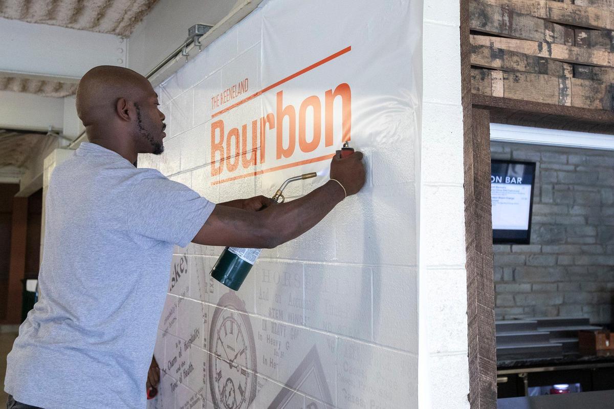 Anthony Adams, of Louisville-based JCGI Graphics and Imaging, applies a vinyl wall mural Wednesday for the new Bourbon Bar at Keeneland.