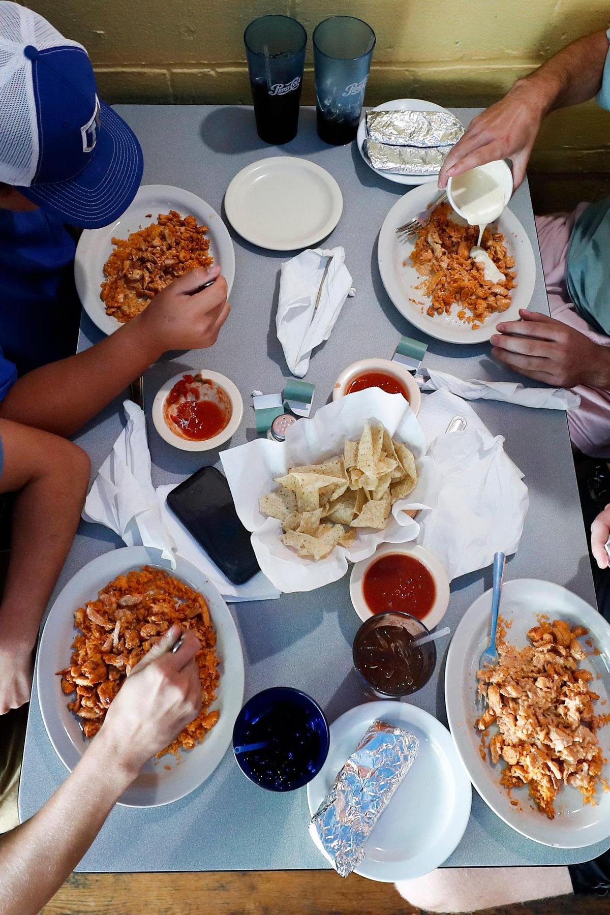 Jared Snapp, clockwise from lower left, Cory Blake, Jeremy Moran and Cameron Dove, all of Paris Ky., eat plates of Famous Town Chicken, which is grilled chicken and cheese sauce served with tortillas and rice at Cilantro Grilled Food and Tacos in Paris, Ky., Friday, July 2, 2021.