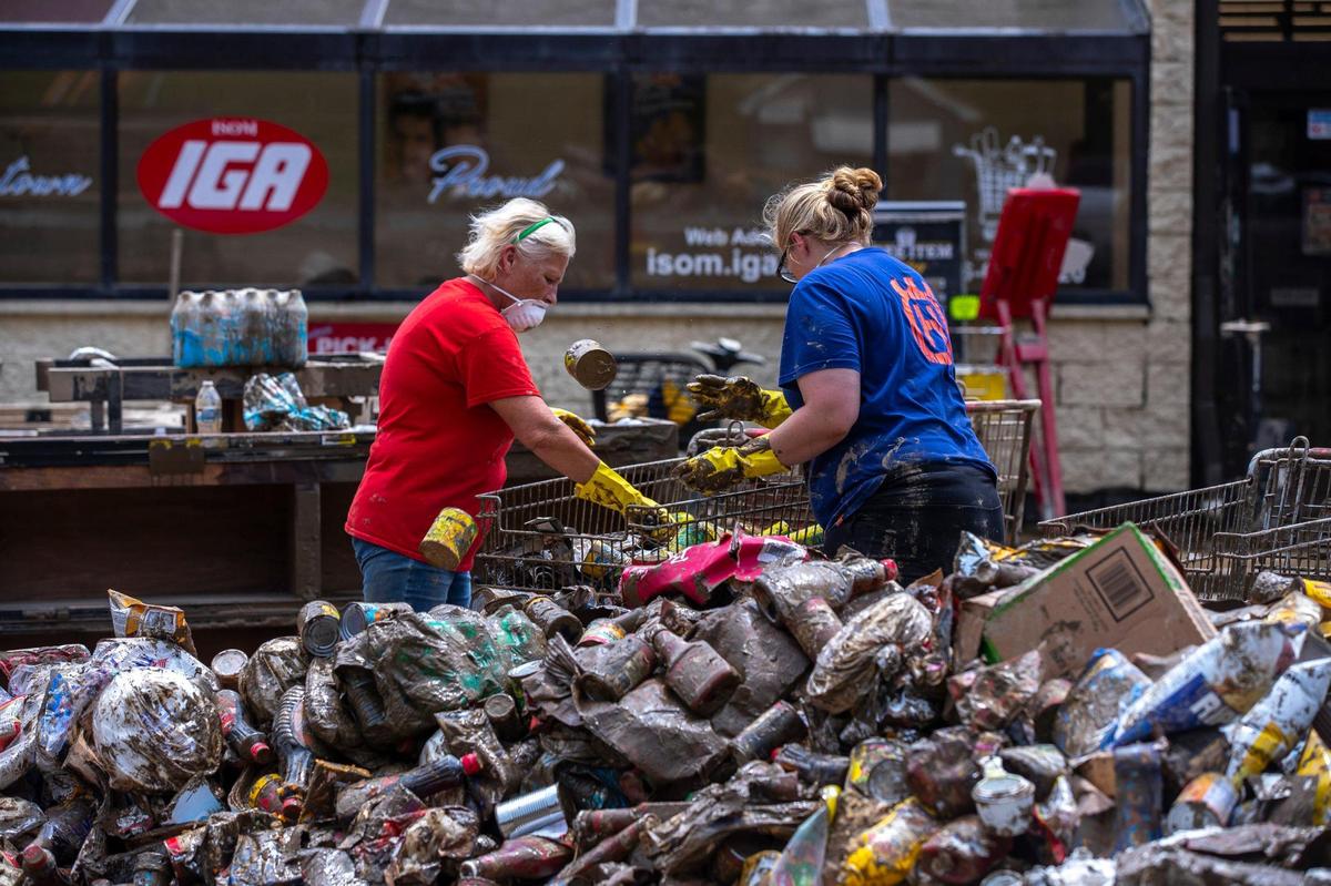 Employees at Isom IGA in Isom, Ky., throw out canned food on Monday, Aug. 1, 2022, after the business was was ravaged by historic floods. The store’s entire inventory was spoiled by the flood waters. After months of cleaning, repairs and rebuilding, the grocery store is scheduled to reopen Saturday, April 1, 2023.