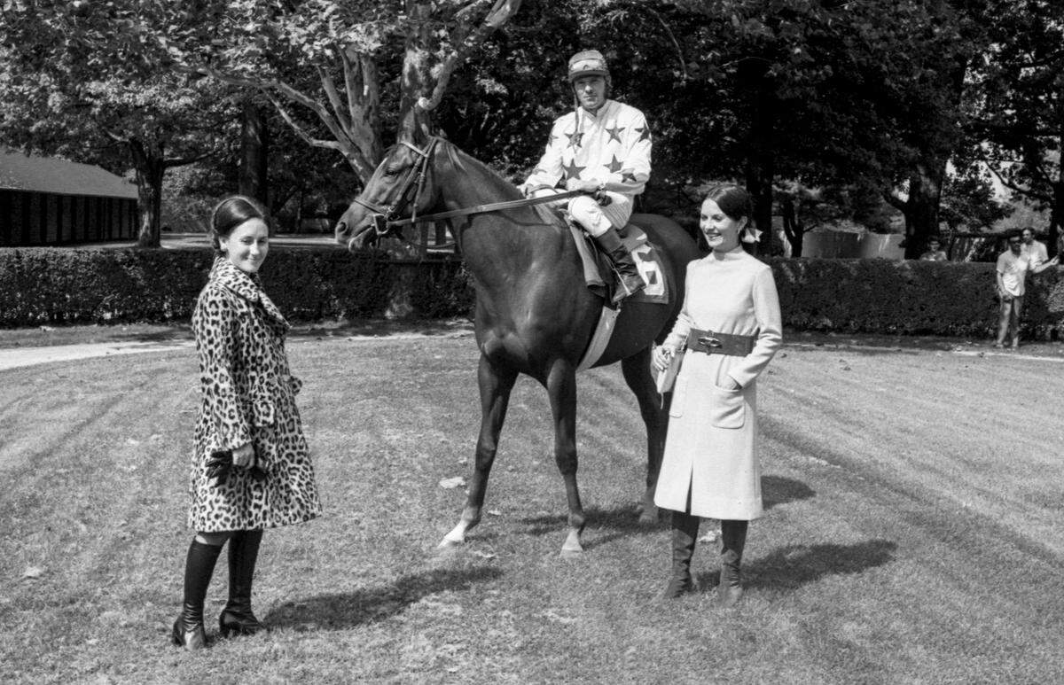 Fashion for the 1971 Keeneland Fall Meet at Keeneland Race Course in Lexington, Ky: Mrs. William Lockridge, left, prepares for the cooler weather in a double-breasted slightly-fitted man-made fur coat. These fabrics are water-repellent and will not shed. Flap pockets detail this coat from Town and Country. Mrs. Hampton Adams Jr. brightens the Keeneland paddock in a yellow wool jersey with wide wine suede belt with large silver buckle by Joan Leslie from Loom and Needle. Dave Burgan is aboard Jenny Song, owned by Mrs. Blanche Kercheval. Published in the October. 10, 1971 Sunday Herald-Leader.