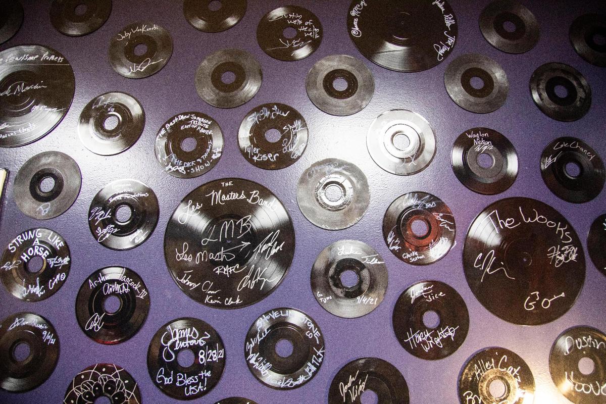 A wall with signed records from artists who played at the Alley on Main hang on a wall by the green rooms for artists.