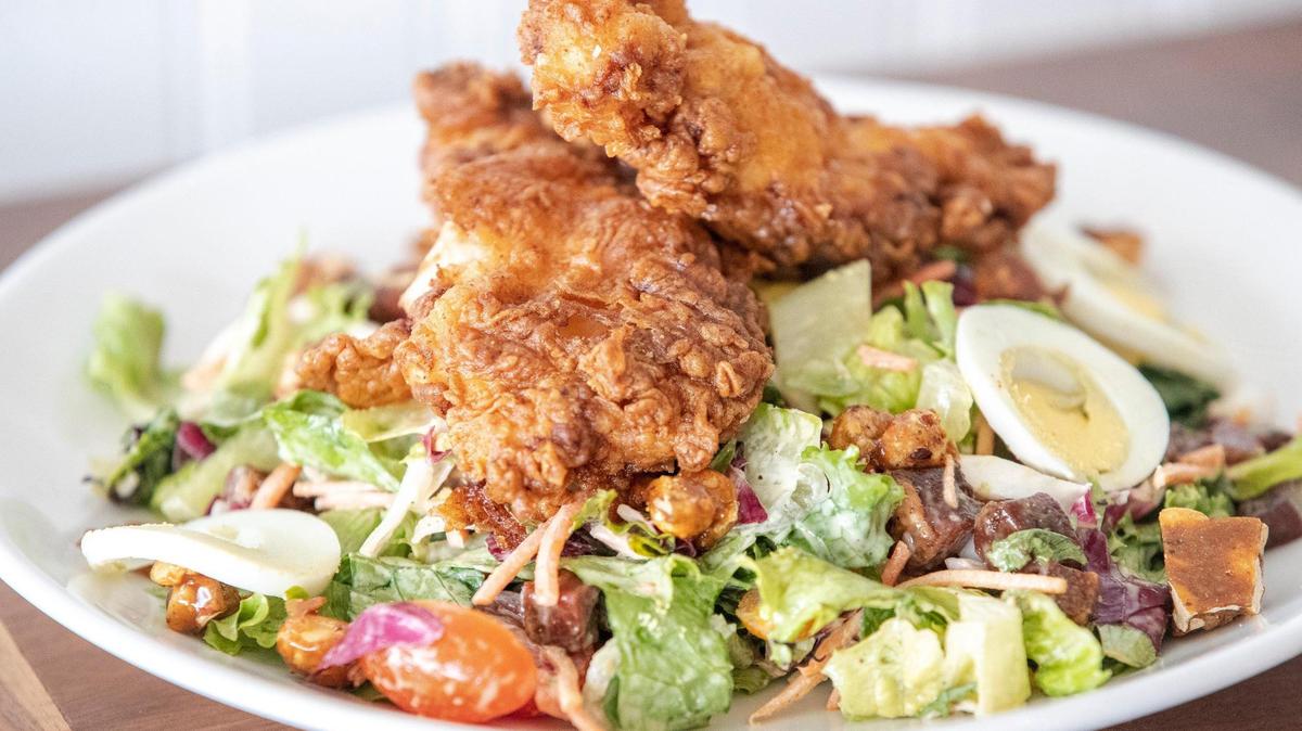 Bella Cafe & Grille’s crispy chicken salad ($16), with mixed greens, heirloom tomatoes, hen’s egg, pancetta, smoked peanuts and honey mustard dressing.
