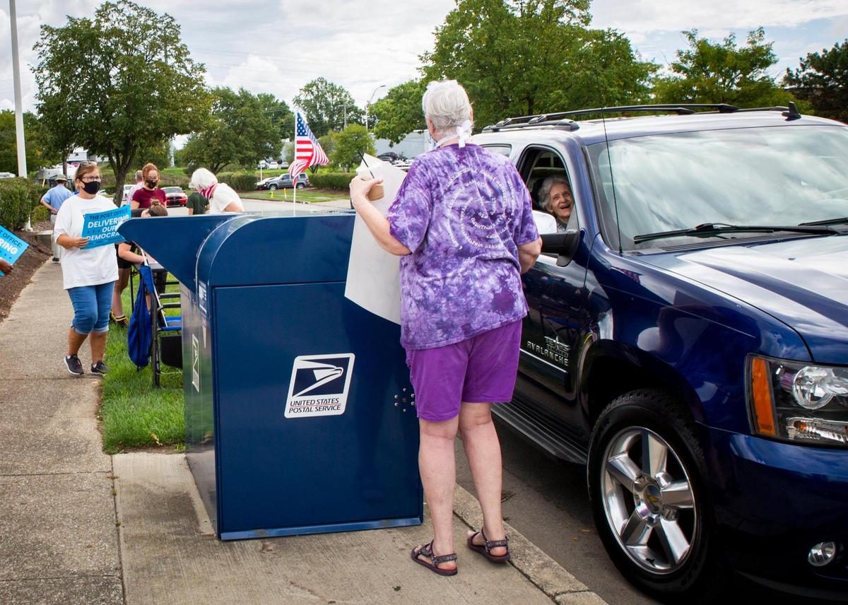A woman dropping off her mail interacts with a protester during the Save the Post Office protest outside the Liberty Road Station post office in Lexington, Ky., on Saturday, August 22, 2020.
