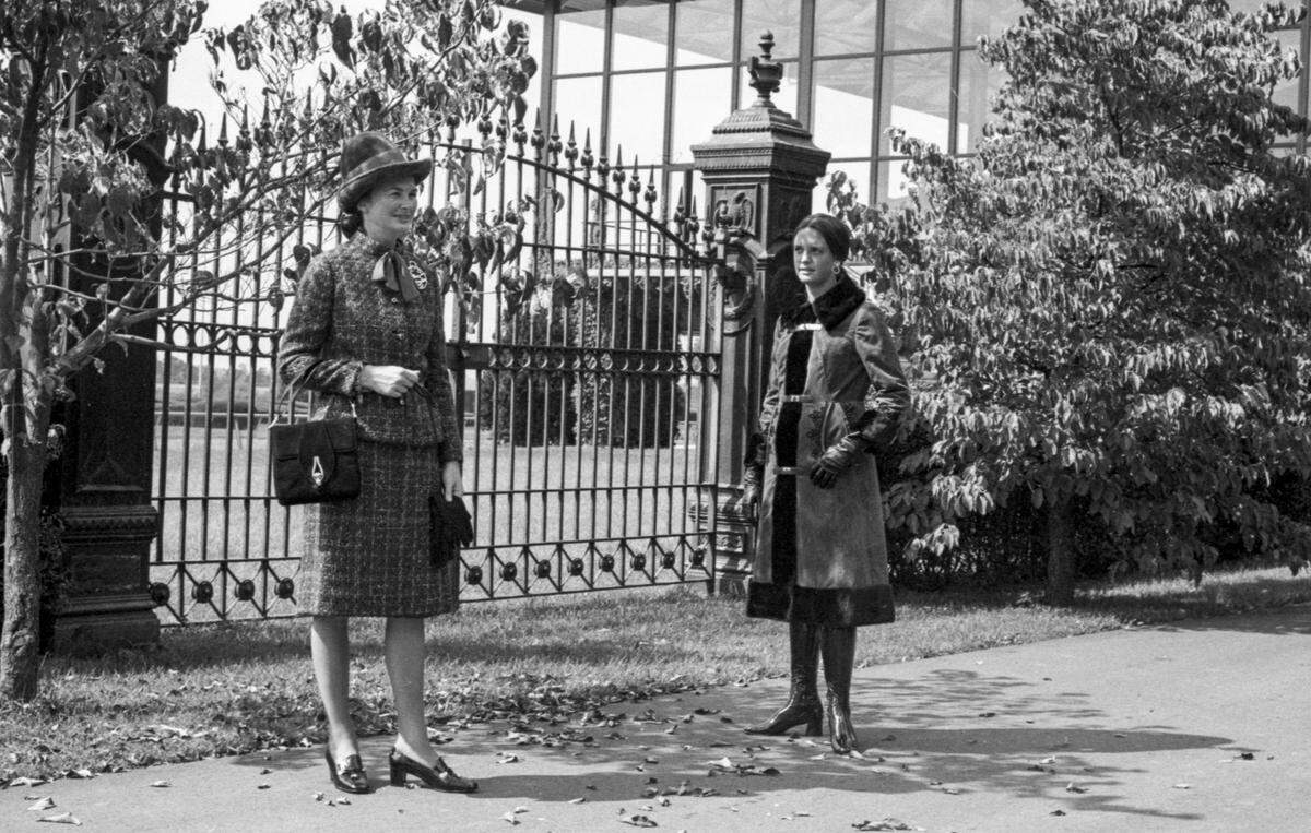 Mrs. John Gaines, left, wears a classic David suit executed in Scottish purple and green tweed with matching purple blouse from Embry’s. Her Tyrolean brim hat is in a wild grape shade. Miss Clay Hancock’s choice for cooler days is a burnt orange fake fur with black trim and leather closings by Natalie Green from Stewarts.