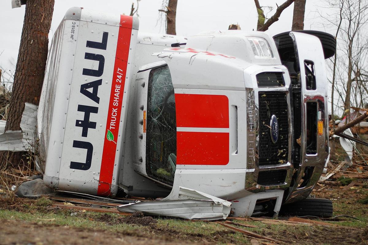 A U-haul box truck sits on its side surrounded by other vehicles and debris in a lot along Paducah Road in Mayfield.
