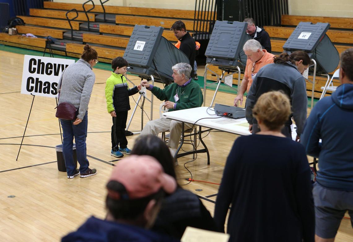 Precinct judge Charles Myers gave a sticker to Henry Kurth, 7, after he watched mom Gena Cooper, left, vote at Chevy Chase precinct Tuesday morning at Morton Middle School.
