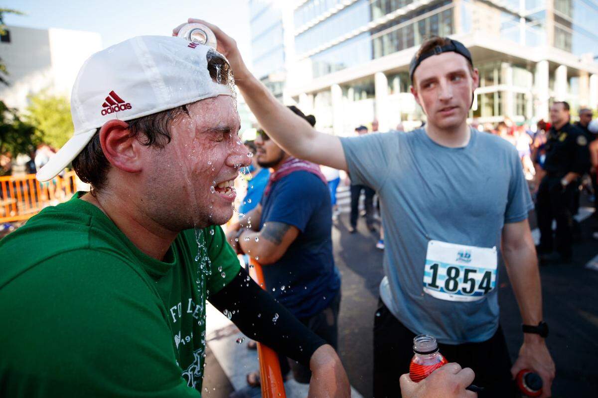 Herald-Leader photographer Silas Walker (right) pours water on the face of Herald-Leader sports reporter Cam Drummond after Monday’s Bluegrass 10,000 in downtown Lexington. Walker finished just ahead of Drummond in the overall finishing order of the race.