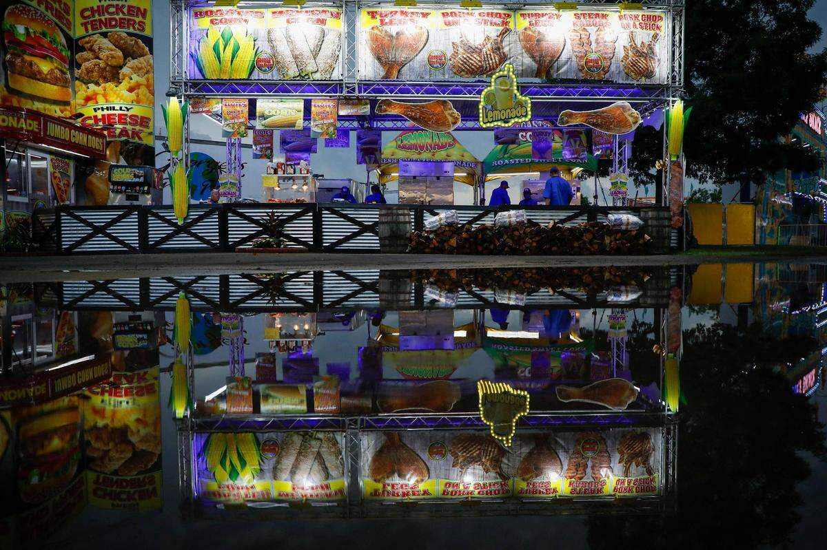 Georges Fun Foods and other food stalls are seen reflected in a puddle at the Lexington Lions Club’s Bluegrass Fair at Masterson Station Park in Lexington, Ky., Friday, June 11, 2021.