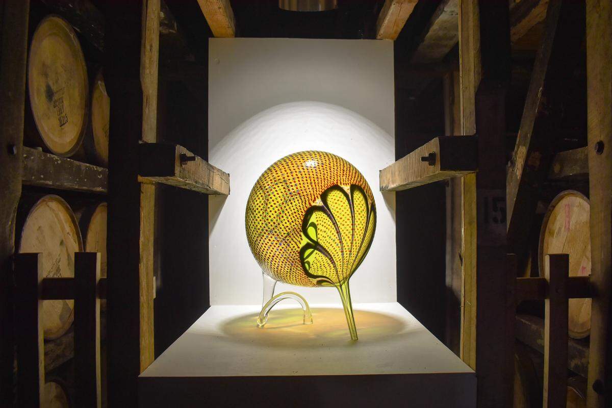 “Acidic Dizzy Snorter,” from Stephen Rolfe Powell’s Whacko series, is displayed in between barrels of bourbon at Makers Mark Distillery in Loretto. The internationally-known glass artist died in March but the exhibit is open thanks to his his students, notes and sketches.
