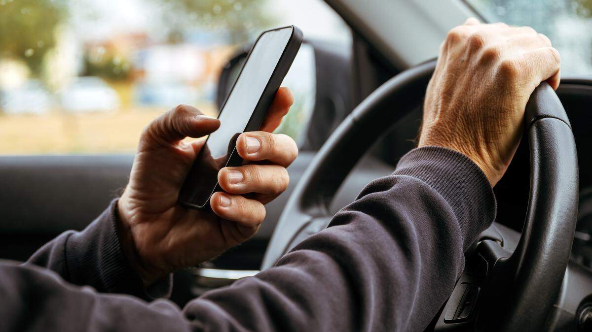 In this stock image, a man texts with a smartphone in one hand and drivers with the other.