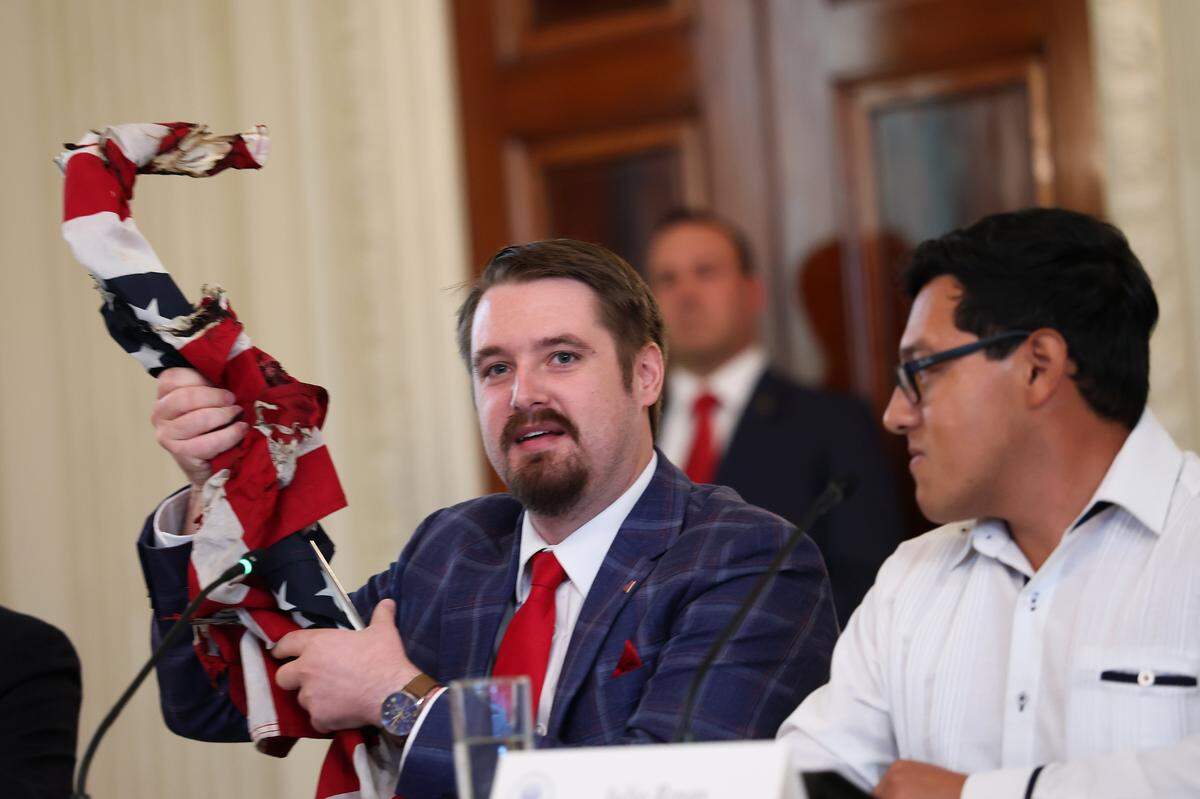 WASHINGTON, DC - OCTOBER 08: Conservative influencer Nick Sortor holds up an American flag recovered from protests in Portland, Oregon during a roundtable discussion in the State Dining Room of the White House on October 08, 2025, in Washington, DC. Trump's administration held the roundtable to discuss the anti-fascist Antifa movement after signing an executive order designating it a domestic terrorist organization. (Photo by Anna Moneymaker/Getty Images)