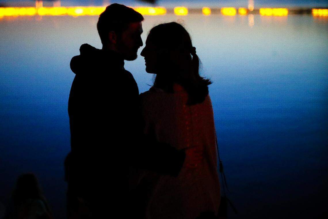 Tyler Clark, left, and Elizabeth Thomas, both of Lexington, Ky., embrace as they watch lanterns collect on the lake during the Water Lantern Festival at Jacobson Park in Lexington, Saturday, June 22, 2019.