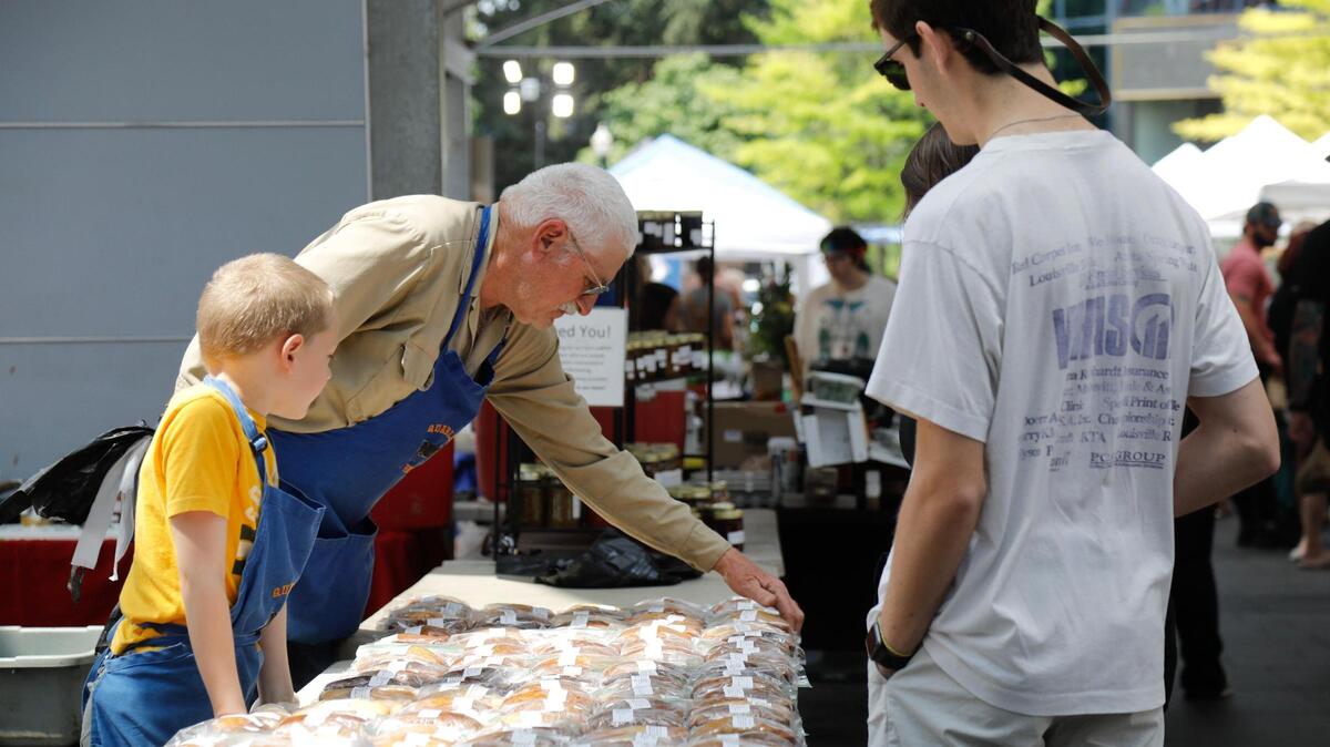 From left, Henry Clary, 8, and his grandfather Paul Quarles sell bread on Saturday, June 24, 2023 at Fifth Third Pavilion in Lexington, Ky. Quarles Farm has not been selected for participation in the 2025 Lexington Farmers Market.