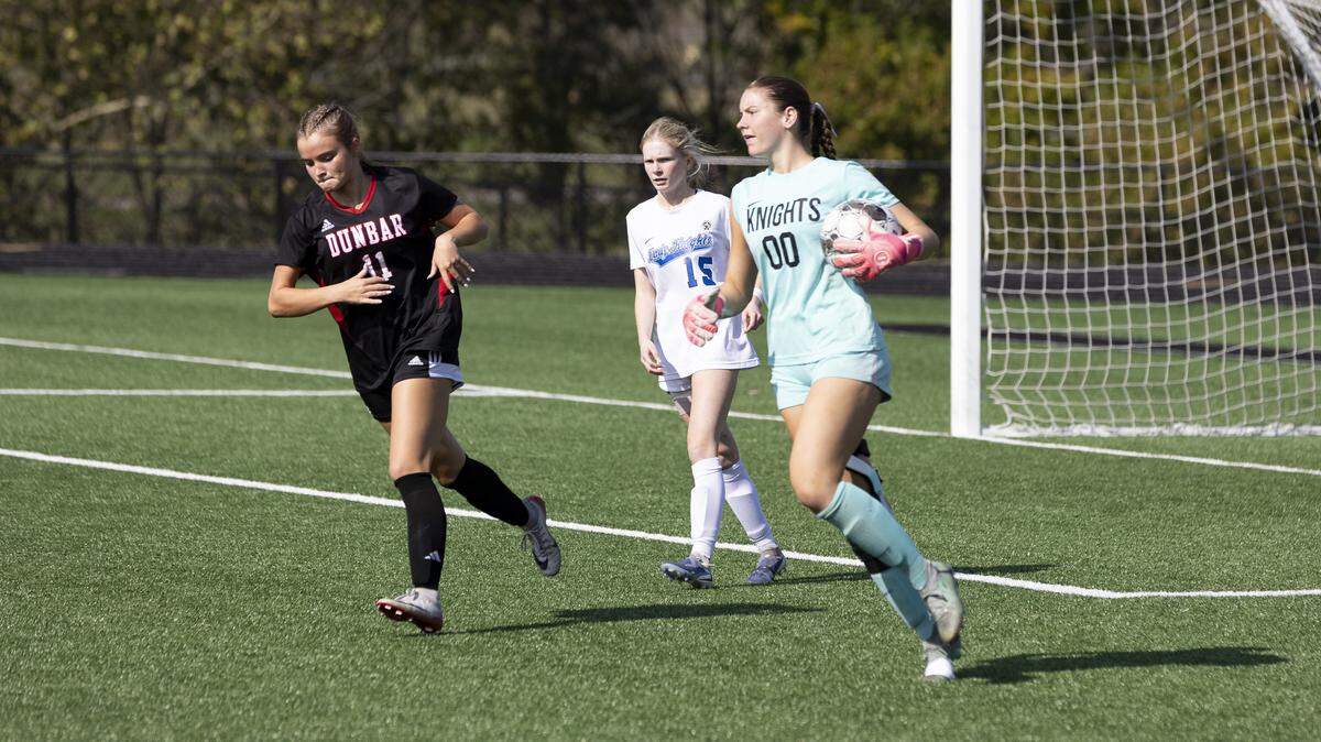 Lexington Catholic keeper Bella Bretz (00) looked up field after collecting a shot attempt in front of Paul Laurence Dunbar’s Layla Flynn (11) and teammate Lily Knopp during the 11th Region girls soccer tournament championship game at Scott County High School in Georgetown on Saturday.