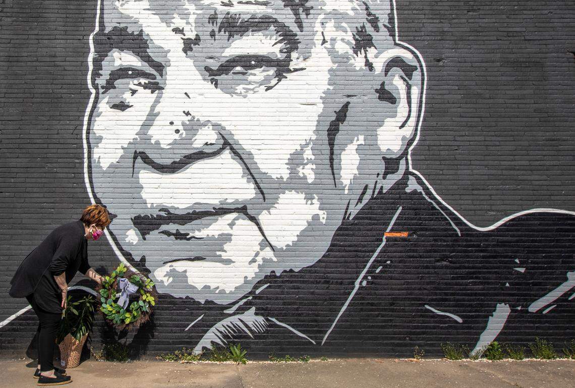 Maribeth Schmitt, of Lexington, Ky., places a wreath below a mural of singer John Prine, on the side of Apollo’s Pizza in Lexington, Ky., on Wednesday, April 8, 2020. Prine, 73, died the day before. The mural was painted last summer by Graham Allen of SquarePegs Studio and Design.