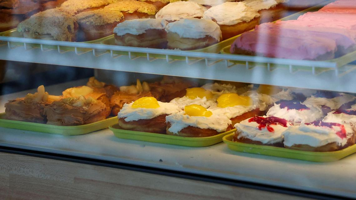 Three different kinds of honeymooner doughnuts in a display case at Jeff’s Donuts, Thursday, Jan. 23, 2025, in Lexington, Ky. A honeymooner is an inside-out filled doughnut without a hole in the middle and capped with specialty toppings. From left is caramel apple, lemon vanilla and cherry vanilla.