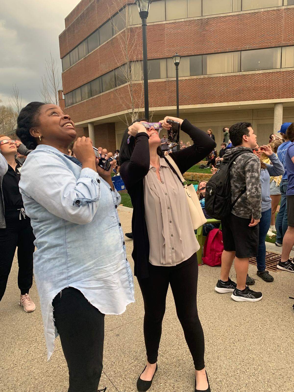 Casey Roley (left) and Michelle Bickerstaff (right) catch a glimpse of the solar eclipse in Lexington amid a cloudy sky on April 8, 2024.