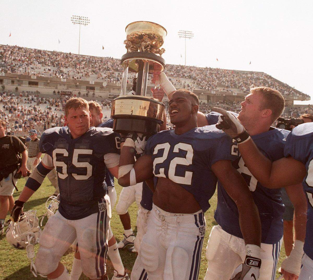 Kentucky’s John Schlarman (65) and Dele Ali (22) carried the Governor’s Cup trophy off the field at Commonwealth Stadium after UK beat Louisville 38-24 in the 1997 season opener.