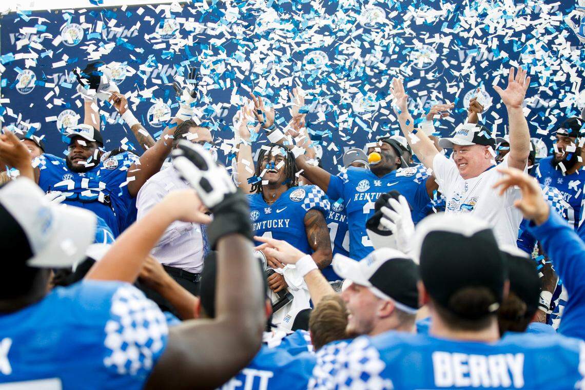 Kentucky’s Wan’Dale Robinson, center, and Cedrick Dort (3) celebrated with head coach Mark Stoops and their teammates after their victory against Iowa in the VRBO Citrus Bowl.