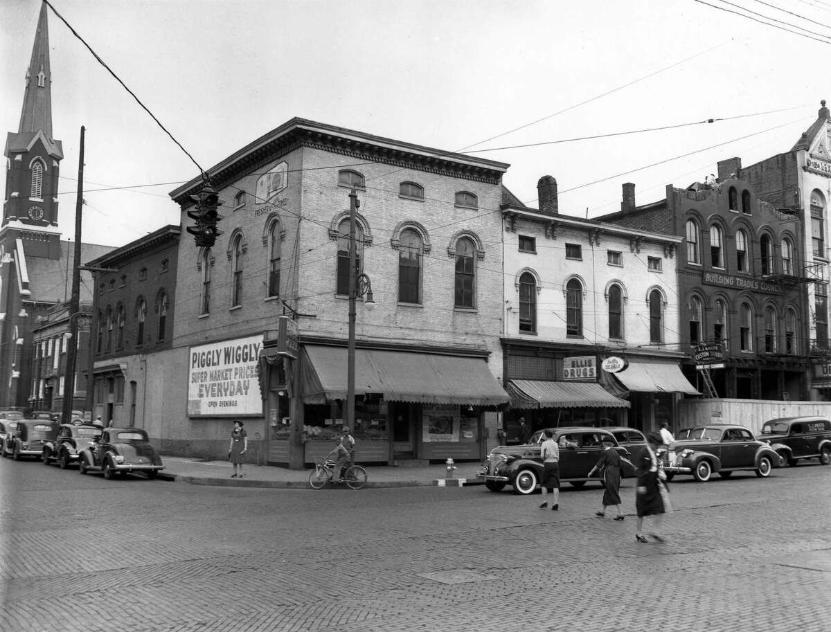 The Piggly Wiggly grocery store in downtown Lexington at the corner of Broadway and Short Street, Oct. 1941. Six months later, two buildings shown here would be torn down and replaced by a new one-story Kroger supermarket. The Kroger featured 5,520 square feet of floor space and a new style of checkout counters. In each of the three lanes, the carts were rolled inside the checking counter so they could be easily reached by the clerks and out of the way of customers.