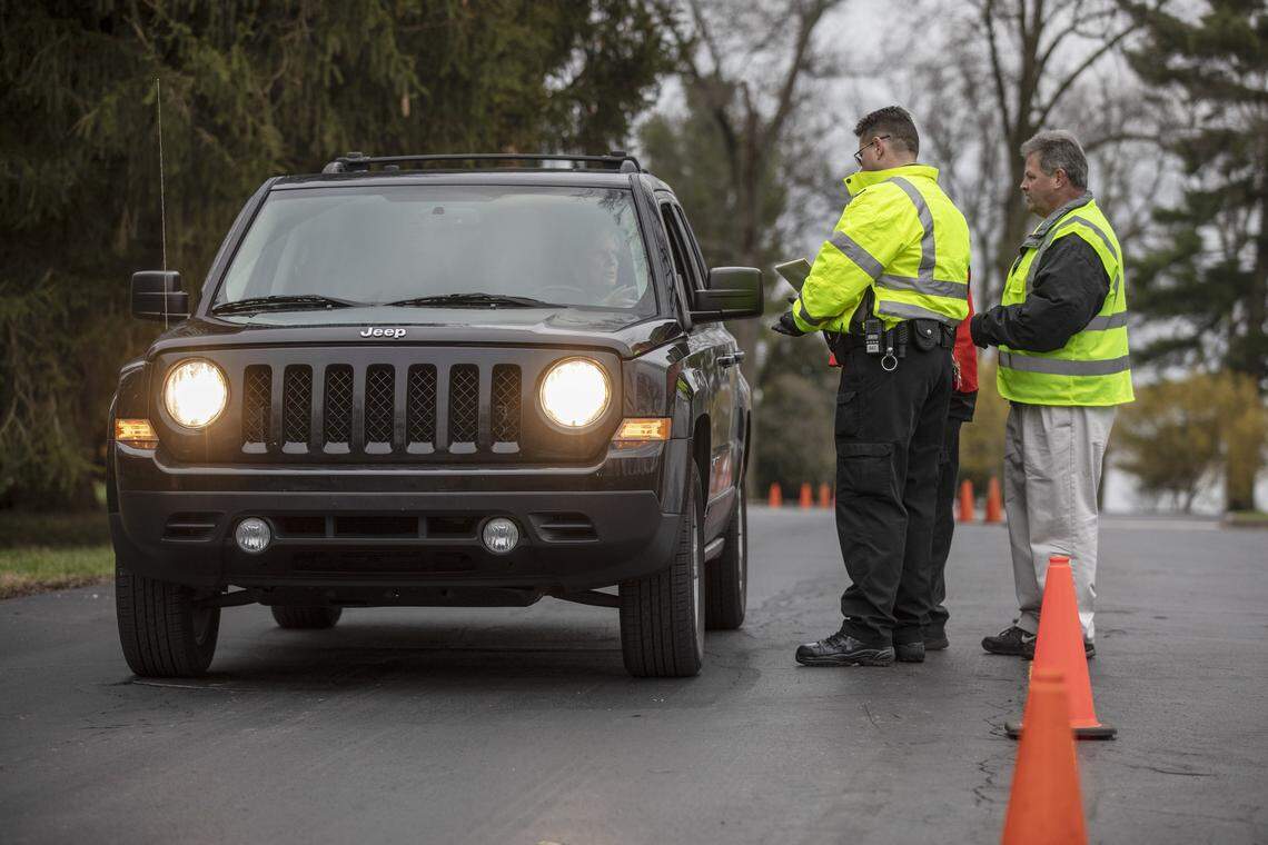 J.C. Stewart, left, and Frank Lea, members of Keeneland security, check a visitor Monday morning at Gate 2. The track is closed to non-essential personnel; authorized owners, trainers, stable workers and veterinarians must pass temperature checks to be allowed on the grounds.