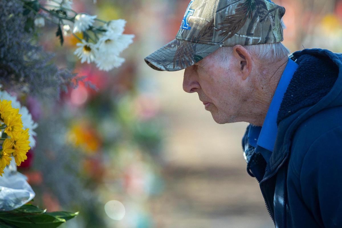 Wayne Rambo looks at photos of victims of the tornadoes that struck Kentucky earlier this month placed with flowers on a temporary fence outside the Graves County Courthouse in Mayfield, Ky., on Monday, Dec. 20, 2021.