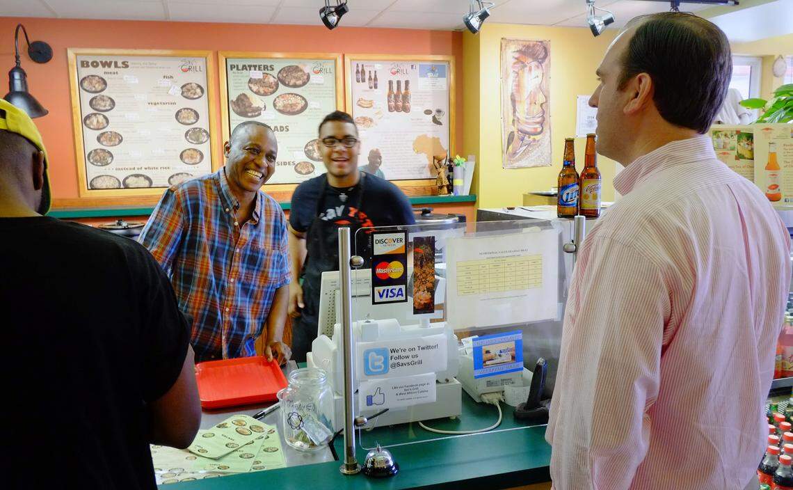 Mamadou “Sav” Savané, left, and his son, Bangaly, greeted customer Mark Hoffman on Tuesday. Hoffman said he had never been to Sav’s Grill & West African Cuisine before reading about Savané’s accident, but “now I’m hooked.” Bangaly Savané’ said Hoffman has become a regular.