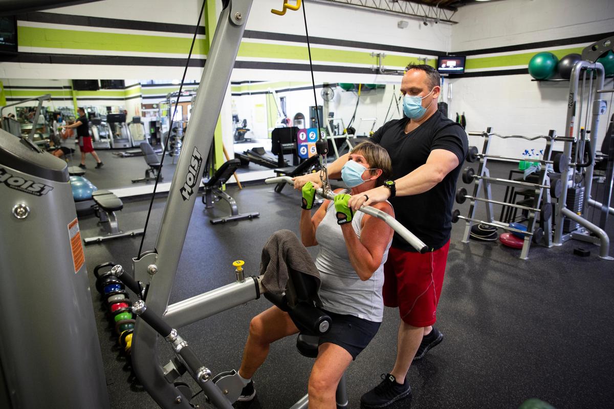 Debbie Feheley worked with her trainer, Chris Williams, while both wore masks at Fitness Plus in Lexington on Monday.