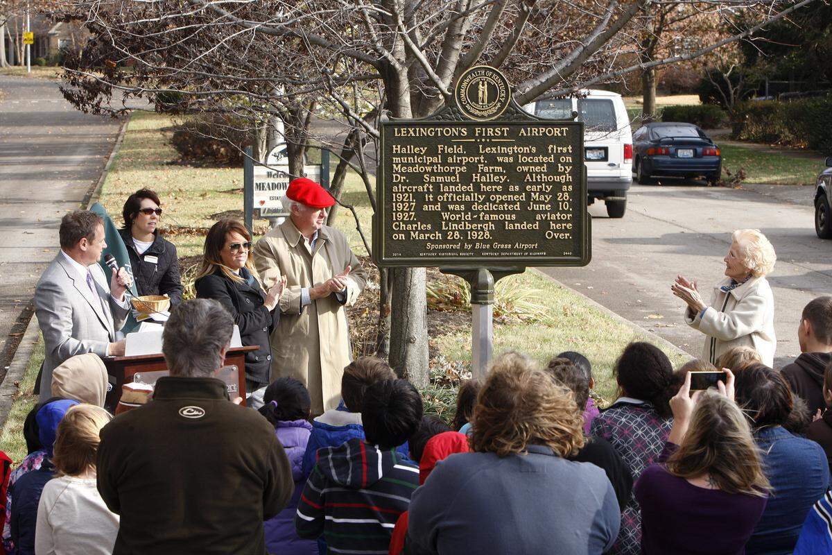 A historical marker on the site of Lexington's first airport was unveiled Monday at Boiling Springs Drive and Leestown Road with help from Sam Halley (red cap), a grandson of the airport's  namesake; Halley's daughter Lyssa McConathy, left of Halley, and Helen Evans, 94, clapping at right, who as a child of 7 was at Halley Field when Charles Lindbergh took off from there in 1928.       