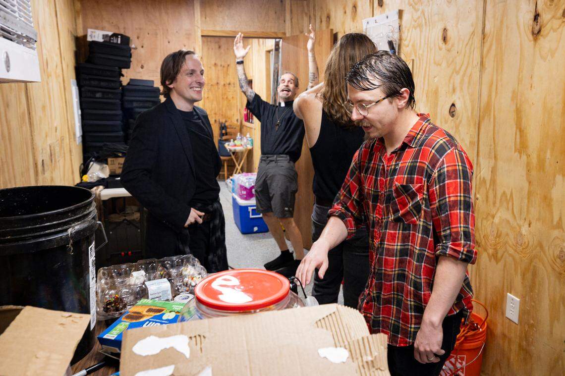 Treyton Blackburn, right, gathers technology in the staging area while it rains outside during the intermission of a showing of Romeo and Juliet on Friday, July 18, 2025, at Woodland Park in Lexington, Ky. Steven Maddox, left, and Adam Luckey, center, celebrate the success of the showing to that point with other cast members.