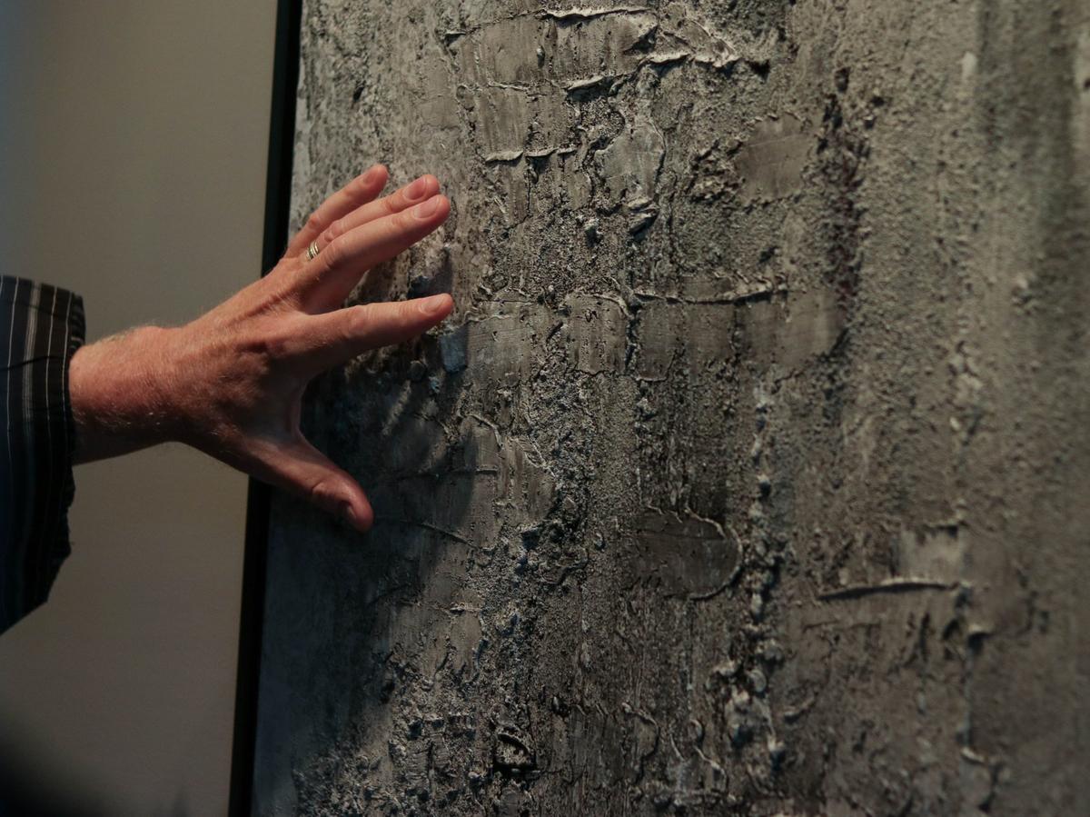 Darrell Ishmael gestures to one of his paintings, which he creates using materials like coal and glass.