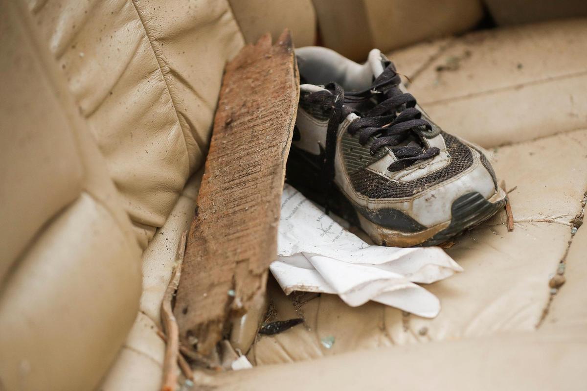 A single right shoe sits in the back seat of a Nissan sedan filled with broken glass and other debris near a destroyed home along North 6th street in Mayfield, Ky.