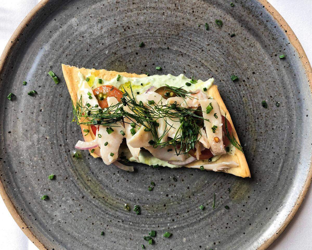 The snack menu at the Tea Dance at Lockbox includes this small plate of house-smoked trout on a crispy cracker with benedictine spread and fresh dill.