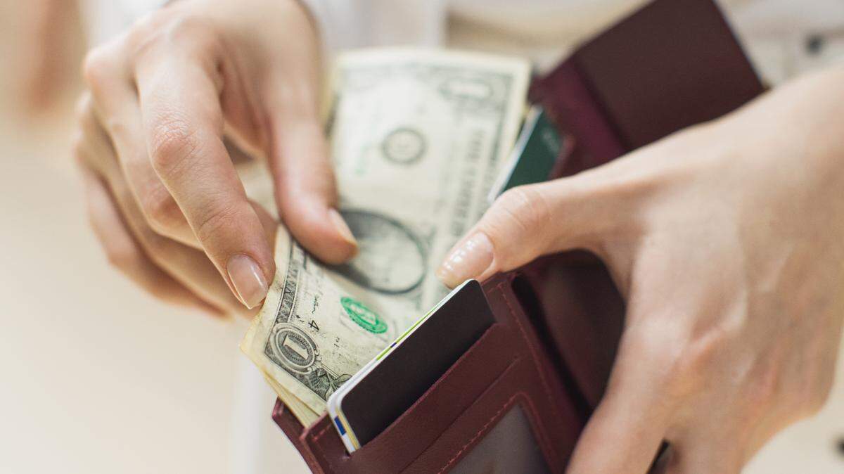 In this stock image, a hand reaches into a wallet for some money.