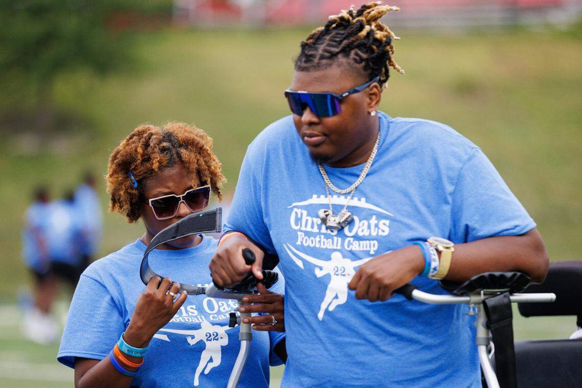 Chris Oats’ aunt, Dorrinna Gamble, fixes the straps on his walker during his football camp on Saturday. A significant portion of the money raised at the camp is going to the Chris Oats Foundation, which was set up to aid him and other young stroke victims.