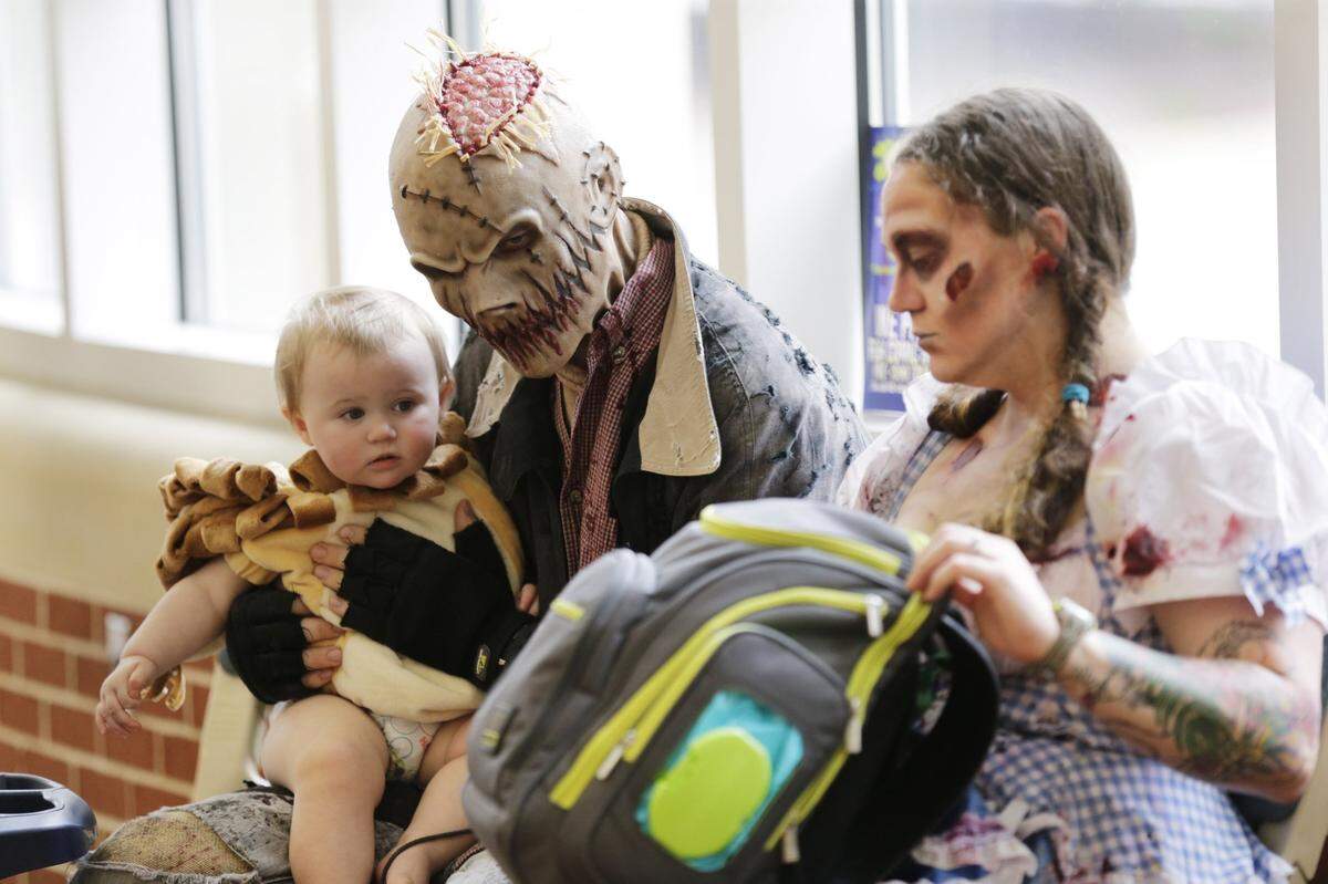 Matt Snider dressed as a scarecrow  held daughter Ellie Snider, a lion,  while mom and fiancee Alicia Reed, dressed as Dorothy, looked through a diaper bag during Camp Scarefest 2016 at the Lexington Center in Lexington, Ky, on Oct. 1, 2016. Snider and Reed work at Wicked World Scaregounds in Lexington where they.  Ellie doesn’t seem to mind her parents costumes.