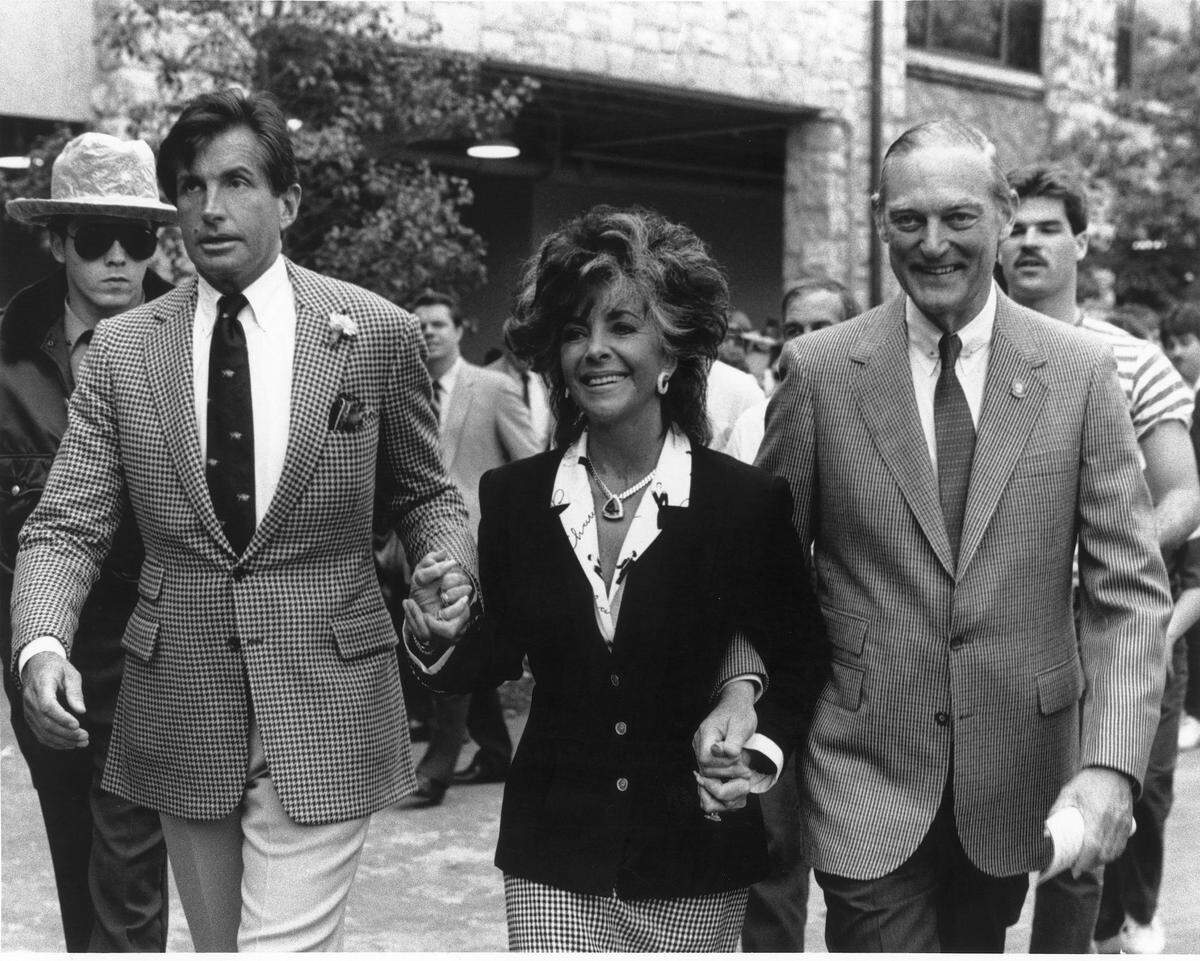 George Hamilton, left, and James E. “Ted” Bassett III, then president of Keeneland, escorted Elizabeth Taylor at the race course on April 5, 1986.