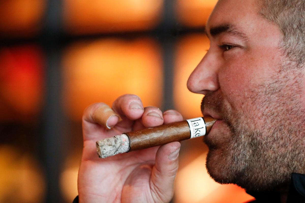 Jake’s Cigar Bar co-owner Jake Glancy smokes the bar’s best seller, a Jake’s White Label cigar.